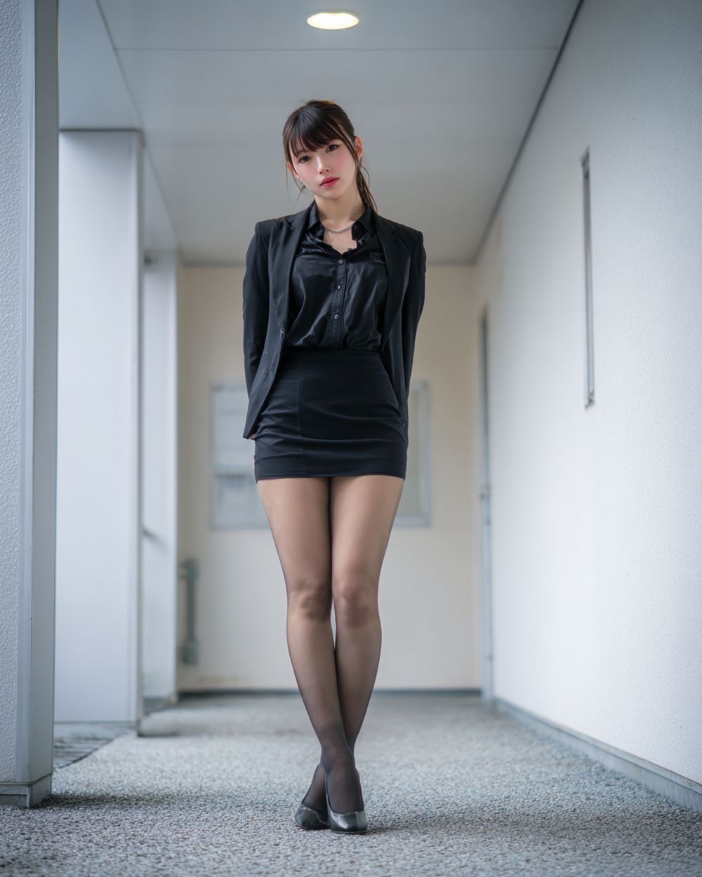 Full body shot of an elegant secretary in a black suit and mini skirt with tights, office corridor.