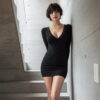 コンクリート階段に立つ黒のミニ丈ニットワンピース姿の大人の女性